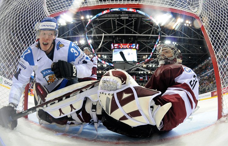 Mika Pyörälä kurkistaa Edgars Masalskisin vartioimaan Latvian maaliin. Kuva: Matthew Manor / HHOF-IIHF Images 110502_HHOF_FIN_LAT_MikaPyorala_EdgarsMasalskis_MatthewManor.jpg